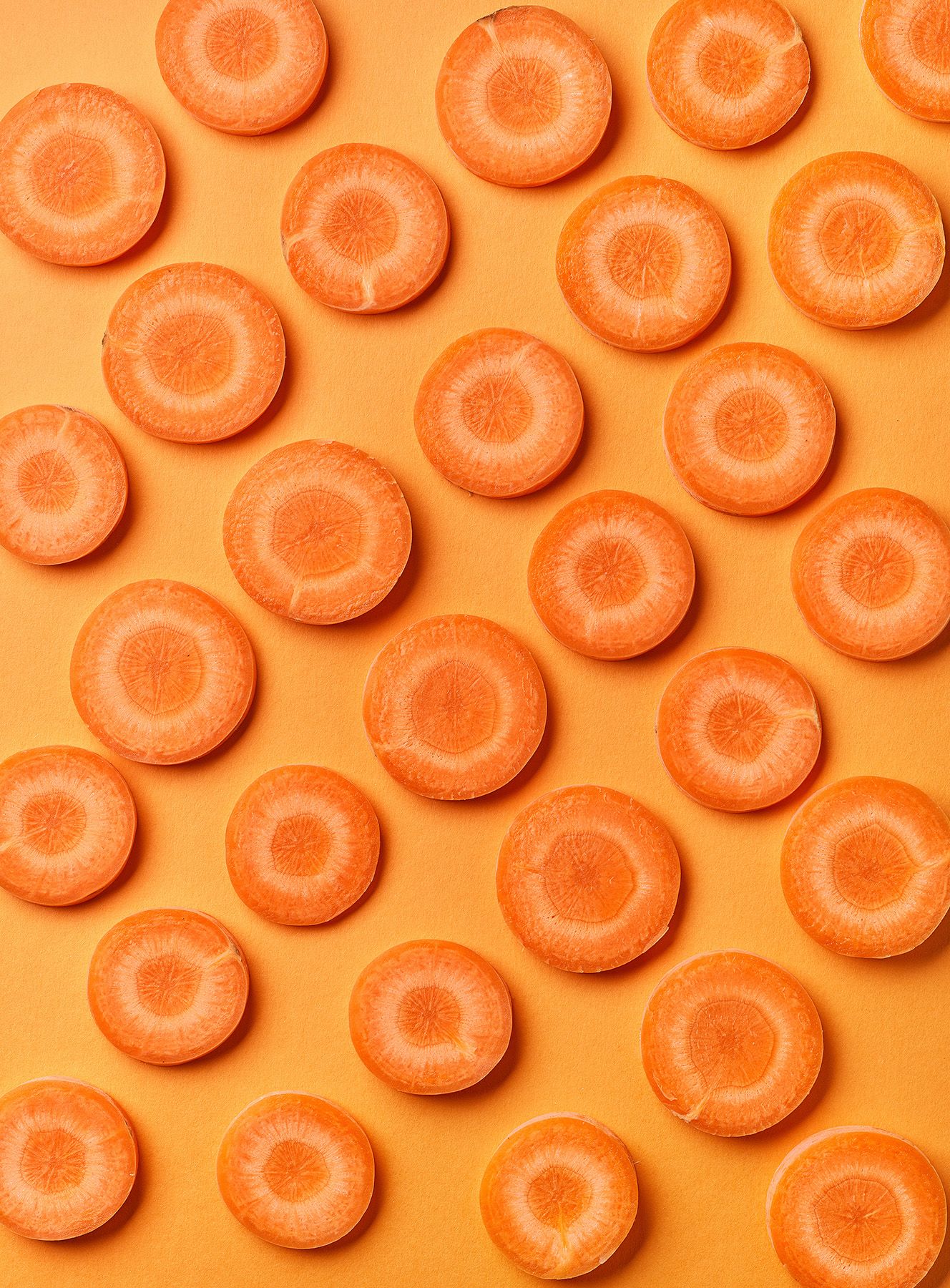 Slices of fresh carrots evenly distributed on an orange background, showcasing a vibrant pattern.