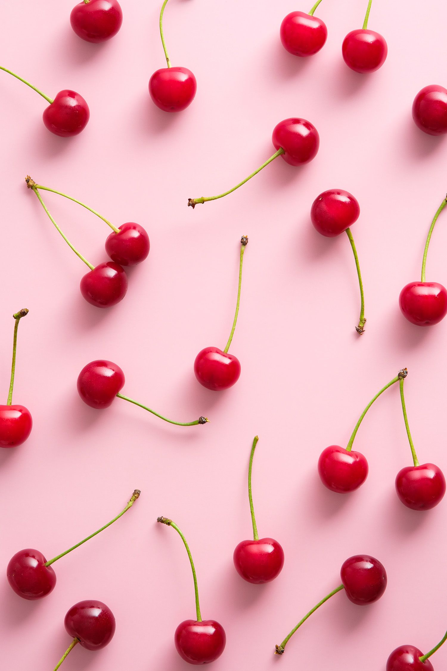 Scattered cherries with stems on a pink background, creating a playful and colorful pattern.