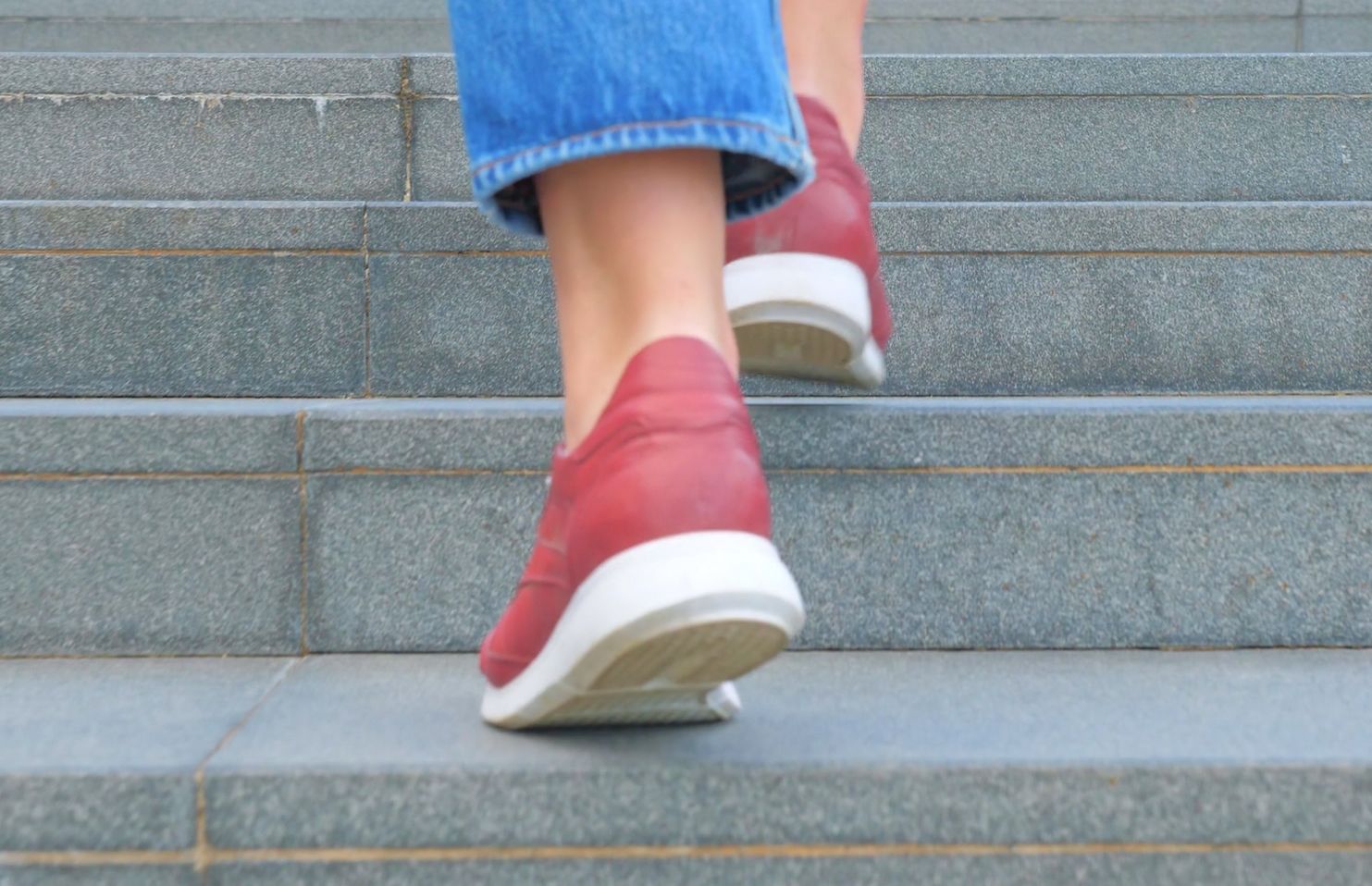 Close-up of a person wearing red shoes and blue jeans walking up concrete steps.