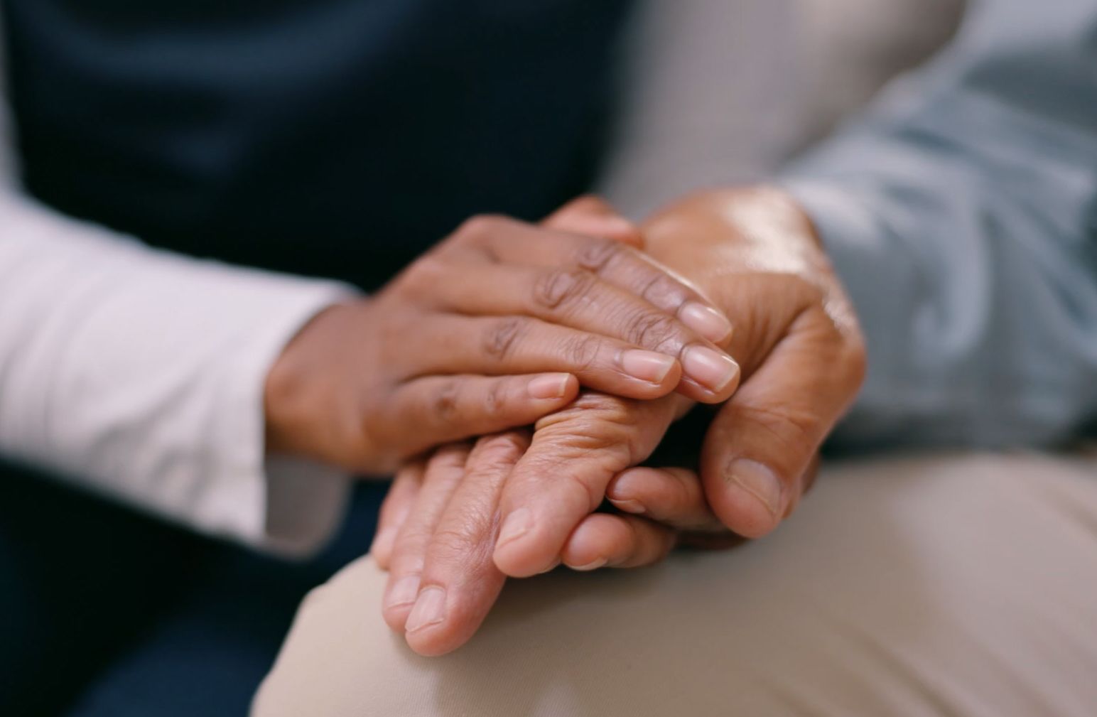 Close-up of a caregiver holding an elderly person's hand, offering comfort and support. The caregiver's hand is gently resting on top of the elderly person's hand.
